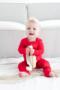 Baby wearing bamboo zip romper in cherry sitting while holding camera toy