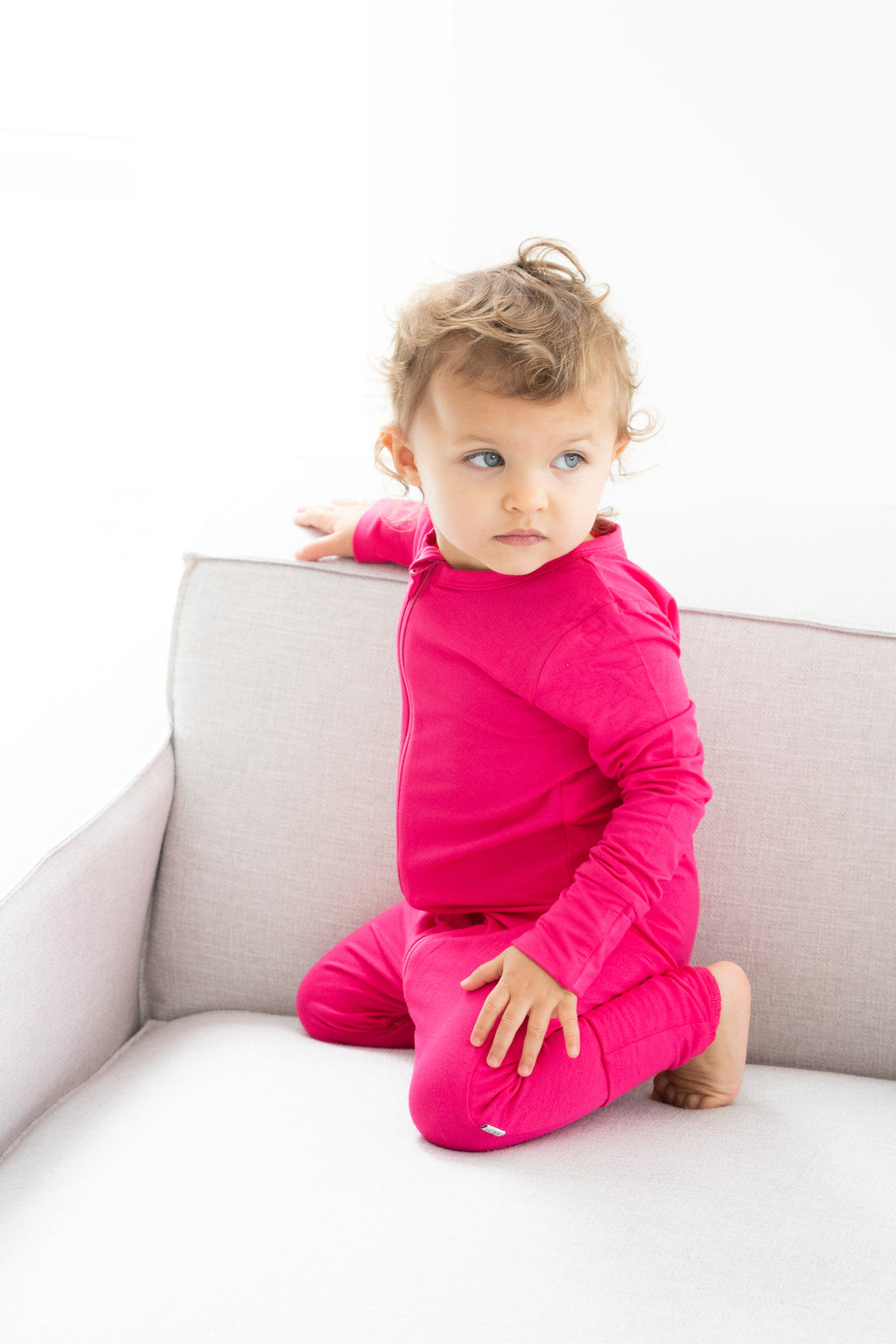 Toddler wearing bamboo zip romper in dragonfruit kneeling on couch