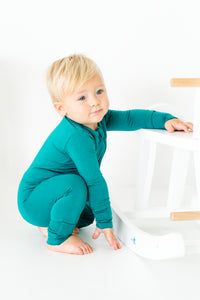 Baby wearing a bamboo zip romper in lagoon, next to rocking horse