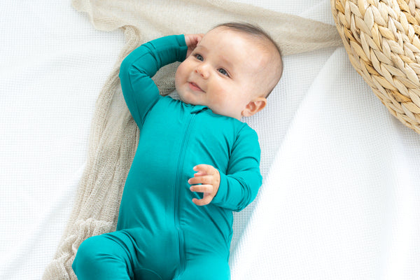 Smiling baby wearing bamboo zip romper in lagoon on beige blanket