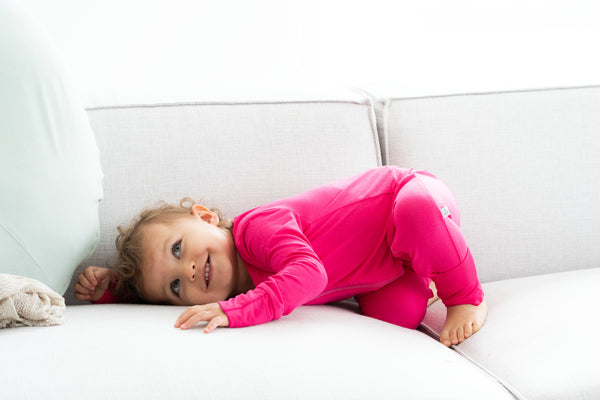 Toddler wearing bamboo zip romper in dragonfruit laying on couch